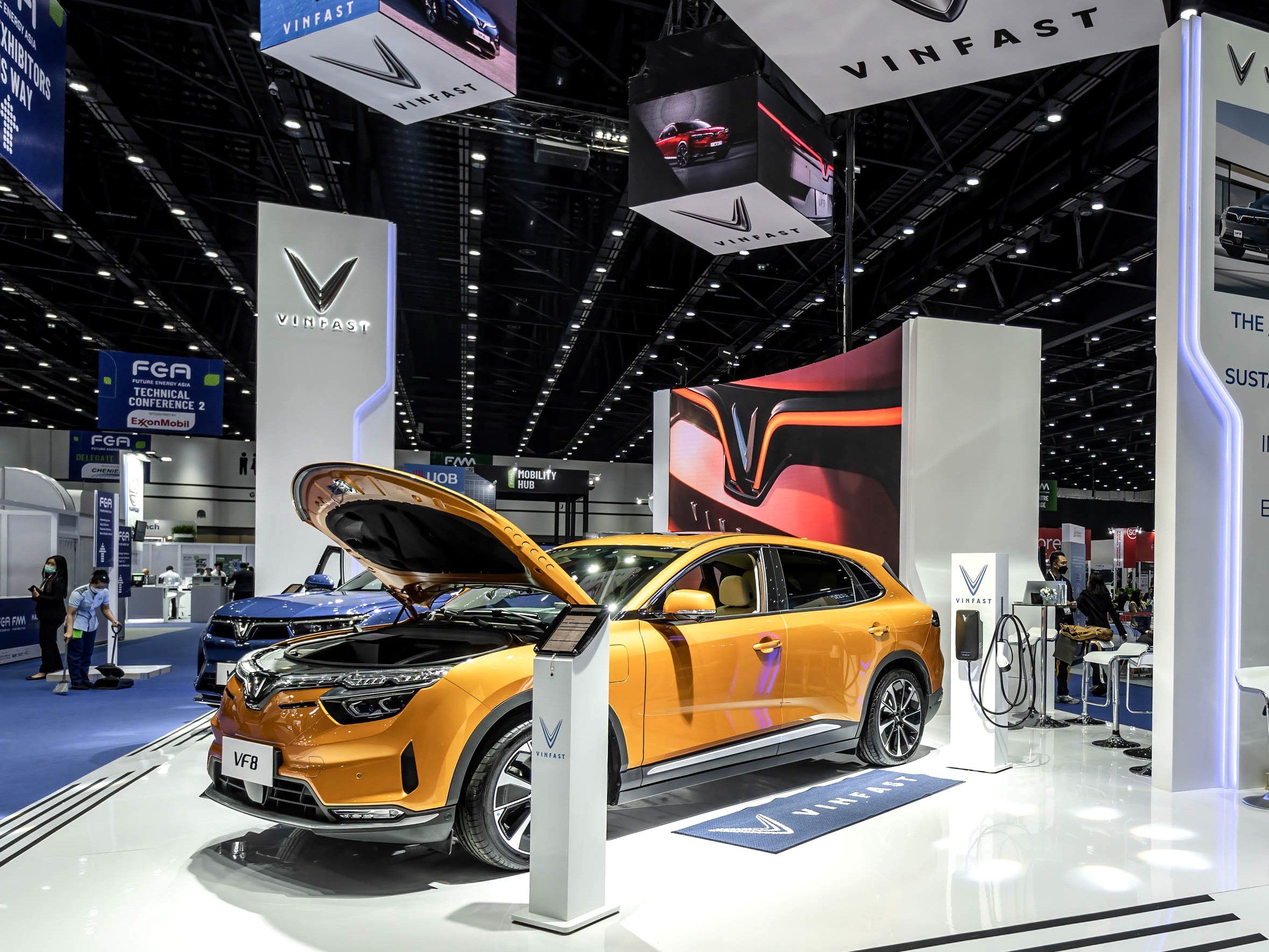 photo of orange electric car in on a white display floor in a large car show exhibition space
