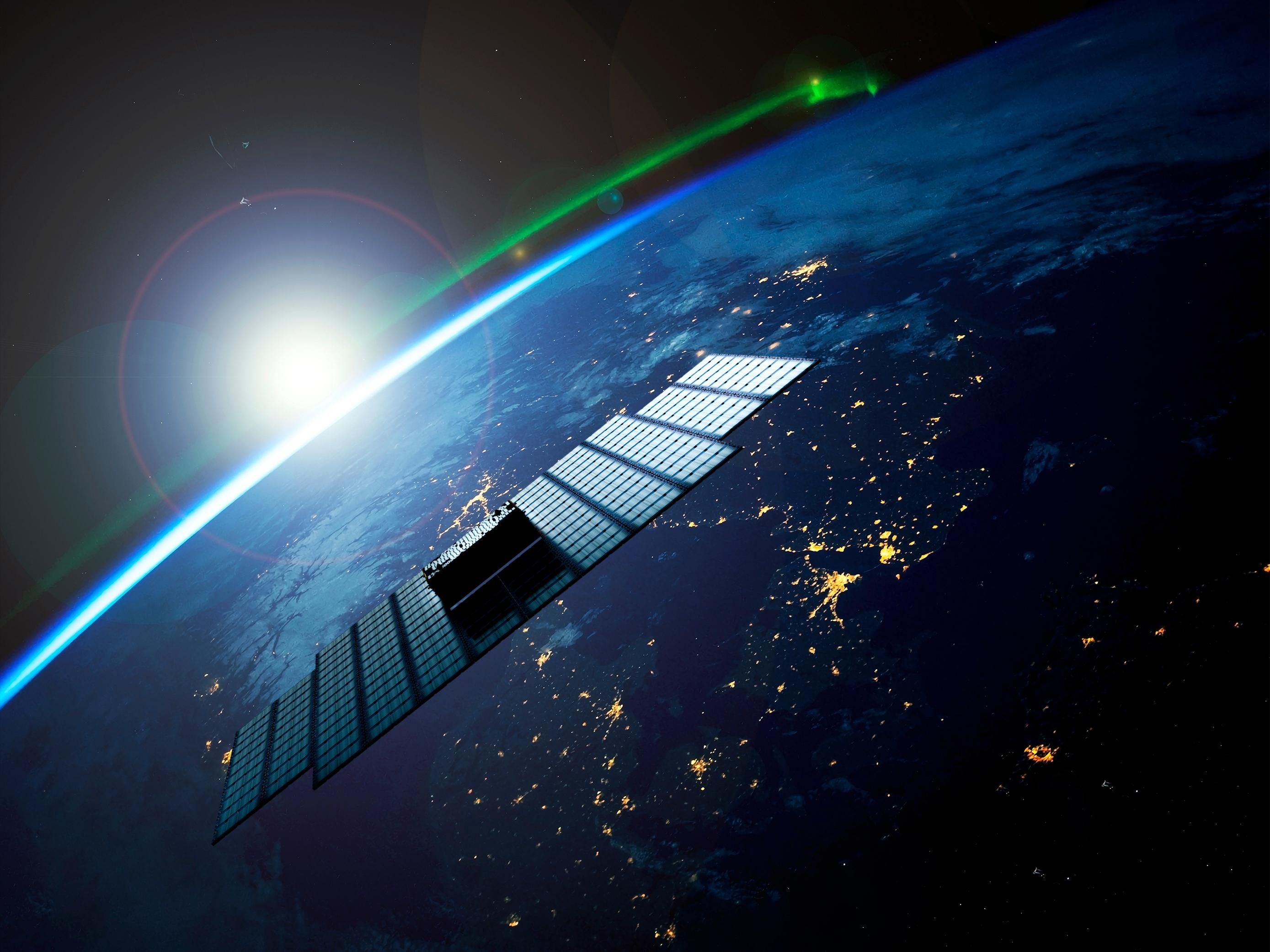 A 3D rendering of a large flat satellite orbiting the Earth, with the sun rising over the horizon behind it.