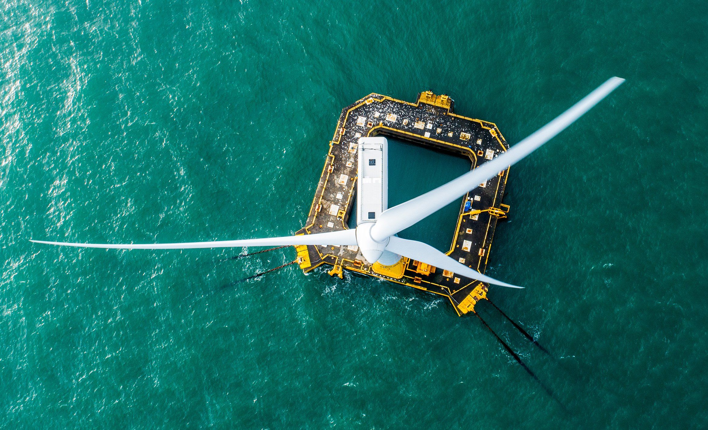 Overhead photo looking down at a wind turbine on a square platform in the ocean.