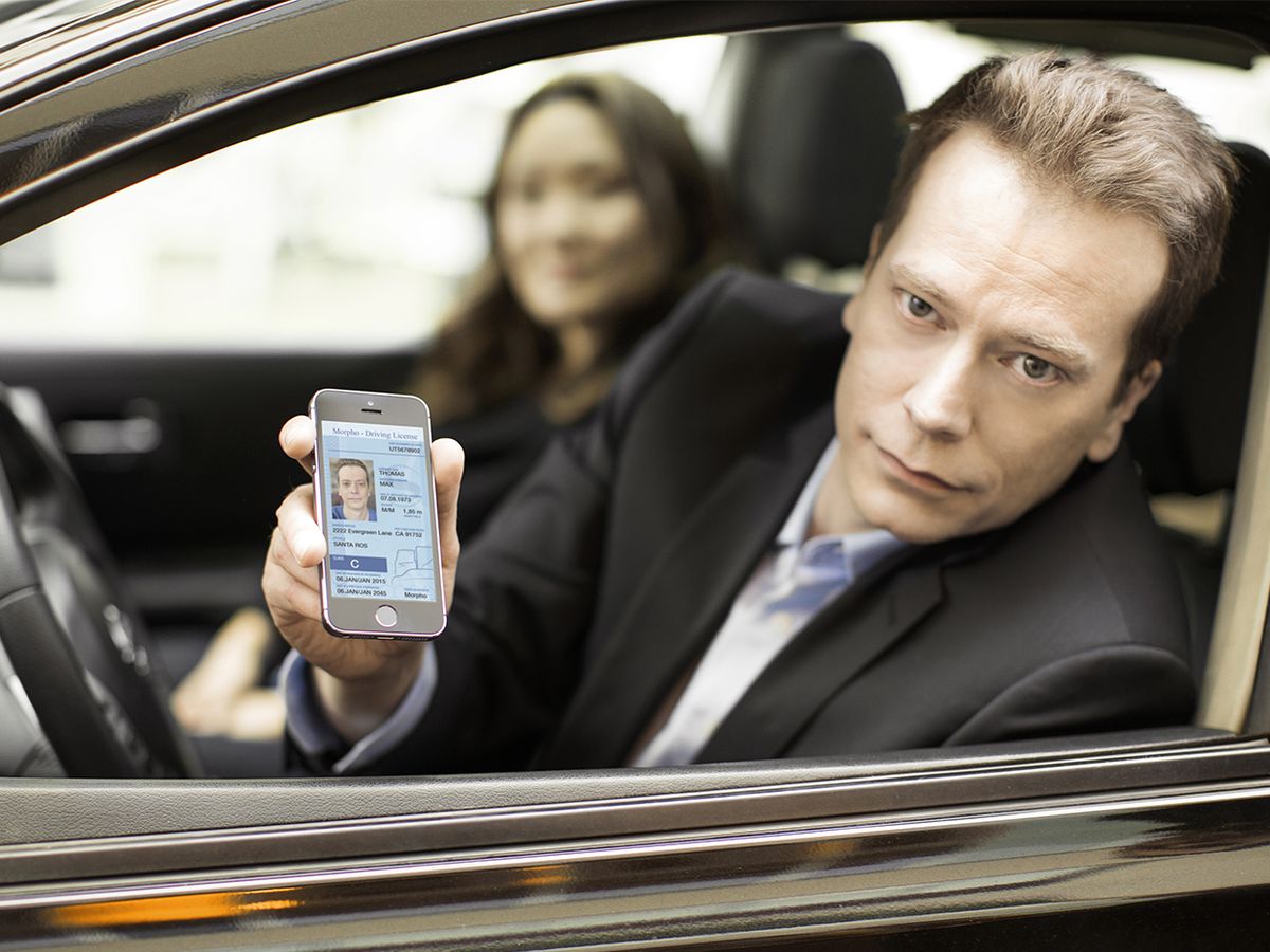 Man in a car showing his drivers license on his phone