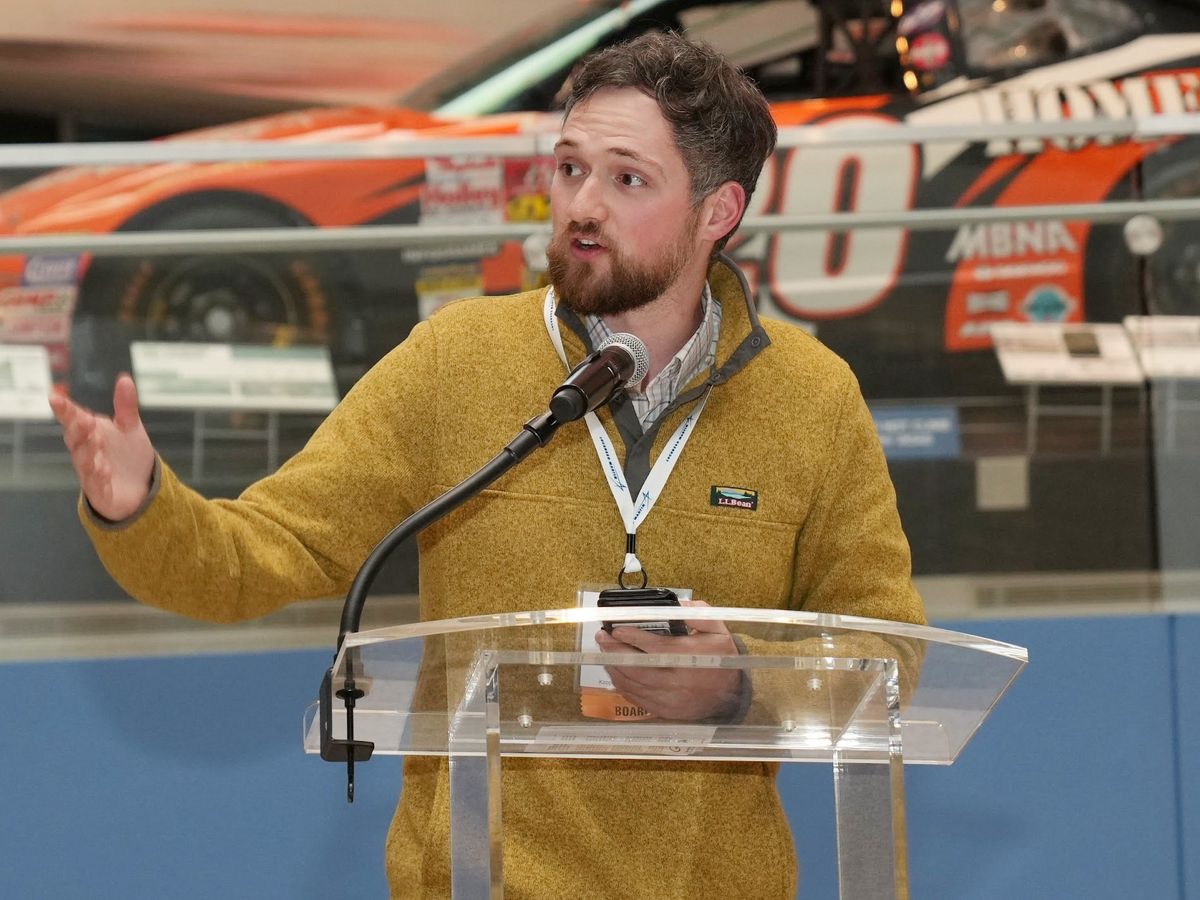 man in a yellow sweater standing at a podium speaking into a microphone  Info for editor if needed: 
