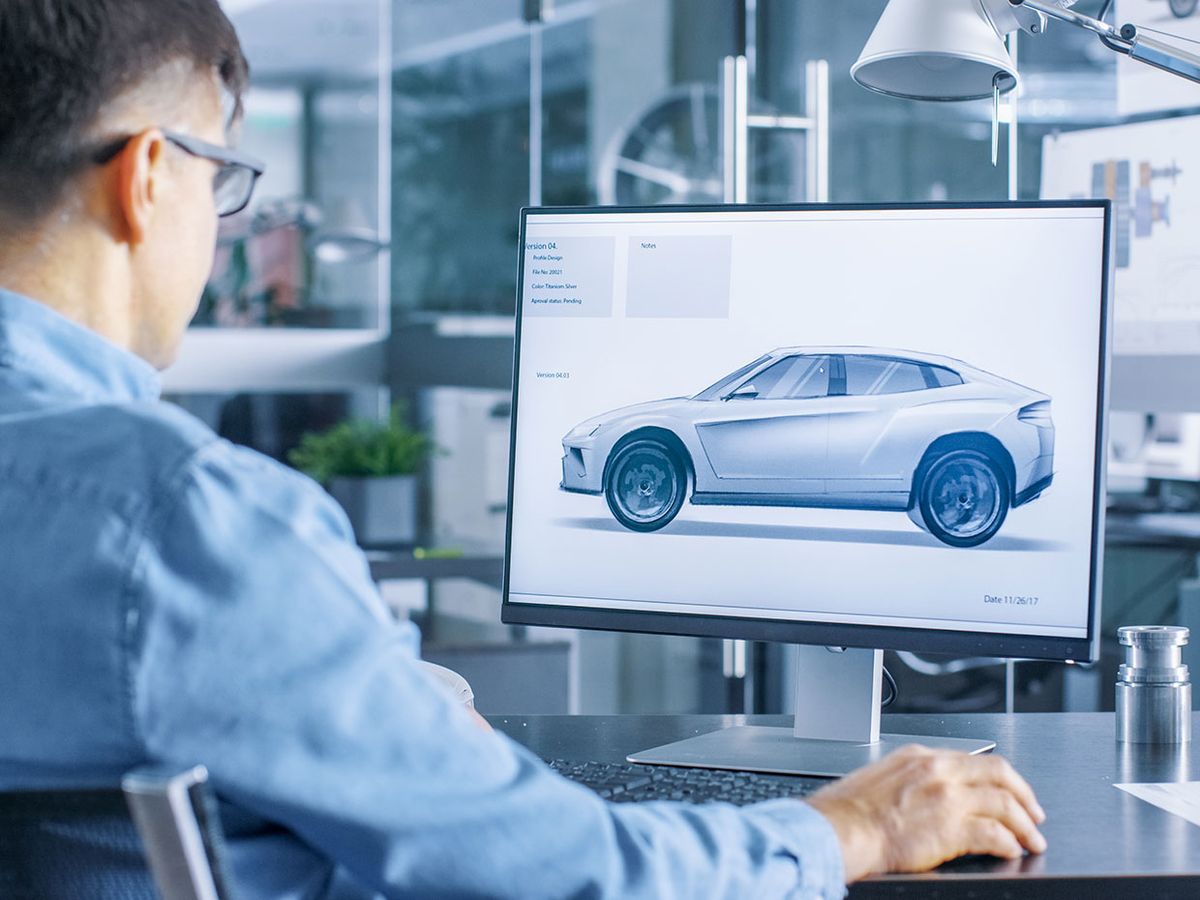 Man in front of a computer monitor with a car design on it.