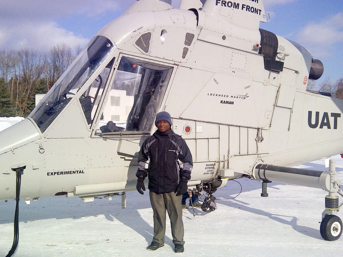 穿着暖和衣服的男子站在一架白色直升机前，地面上有雪