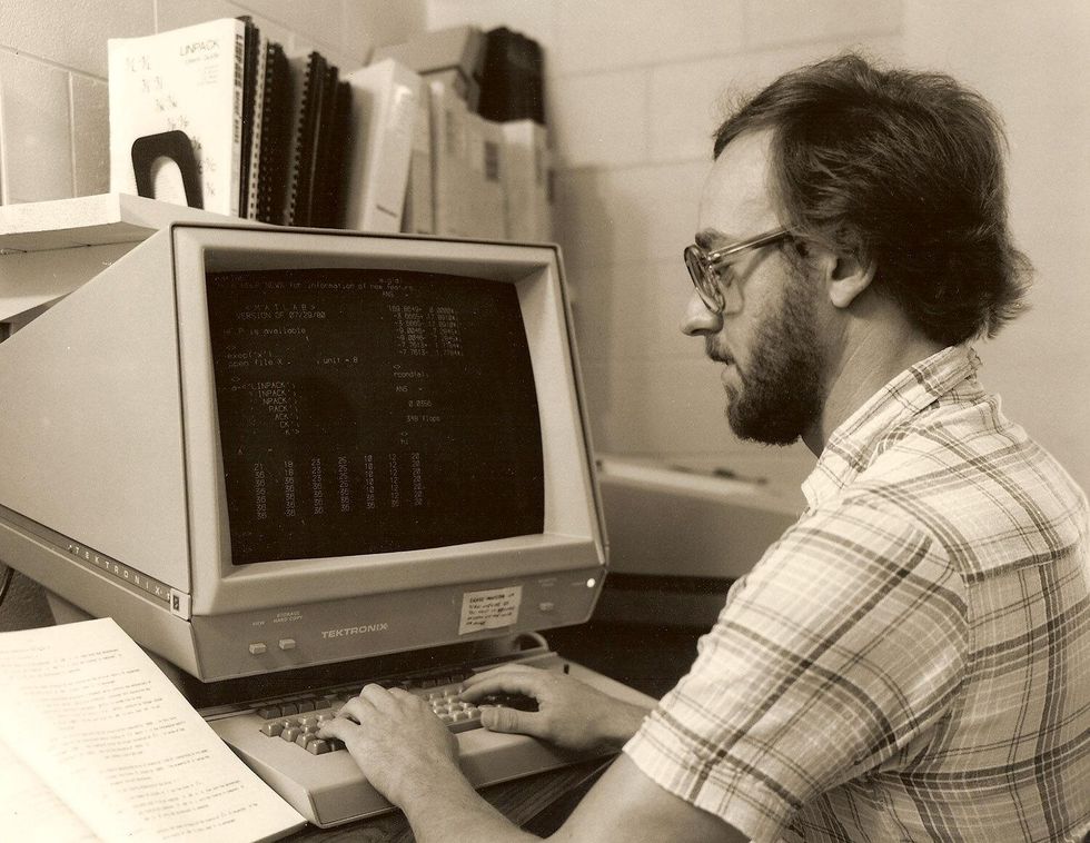 Homme avec des lunettes et une chemise à carreaux assis devant un ordinateur Tektronix.