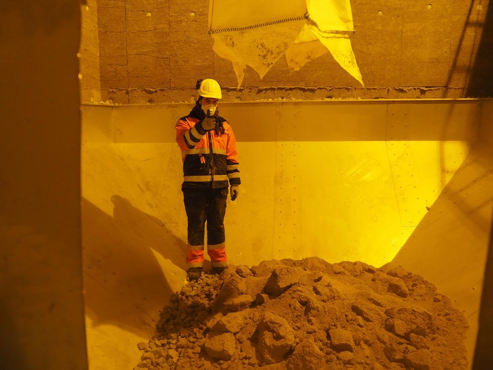 Markku Yl\u00f6nen dressed in construction gear stands inside a pile of sand-like dirt.