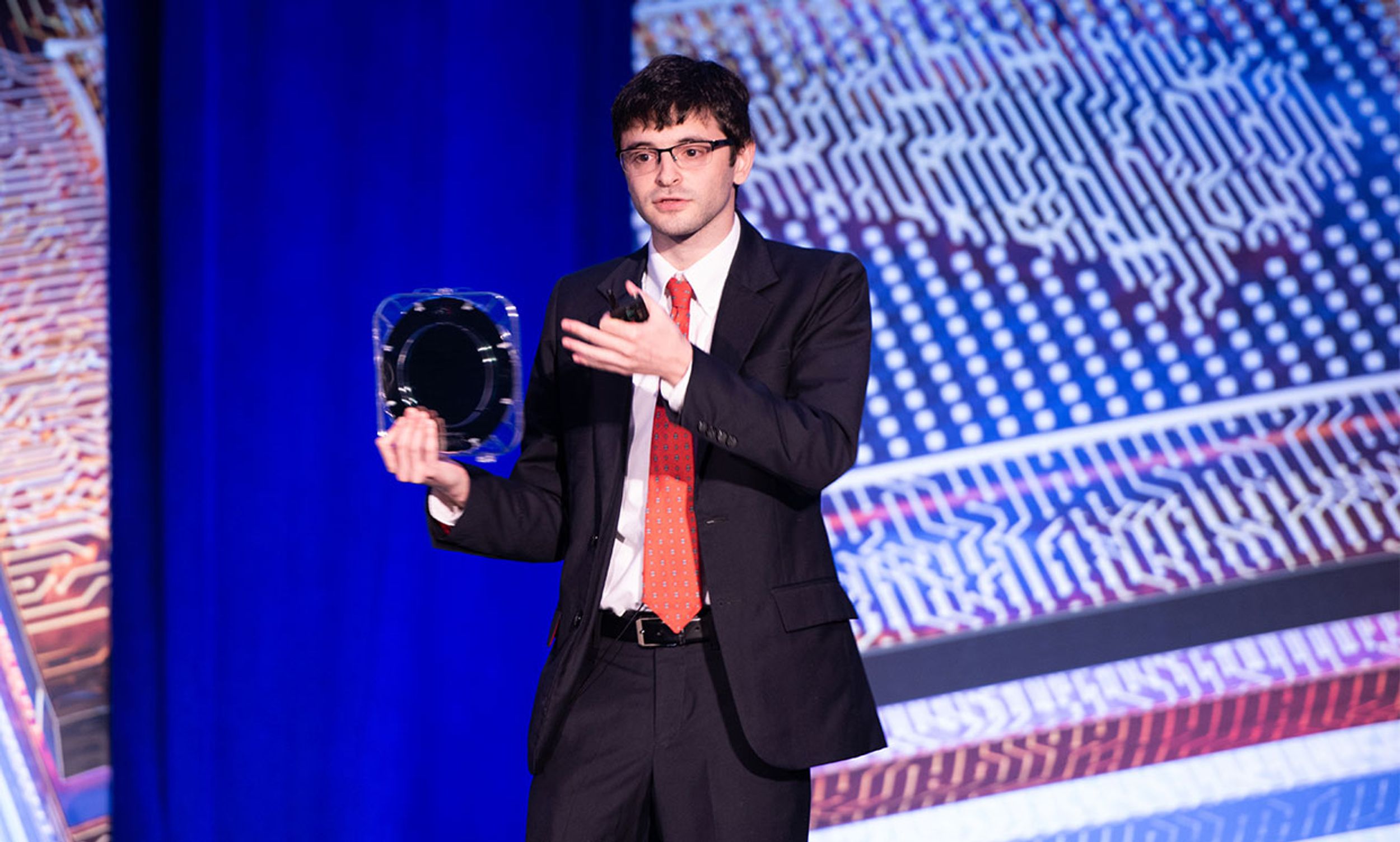 MIT assistant professor Max Shulaker holds up the first foundry-built monolithic 3D carbon nanotube IC at the DARPA Electronics Resurgence Initiative Summit.