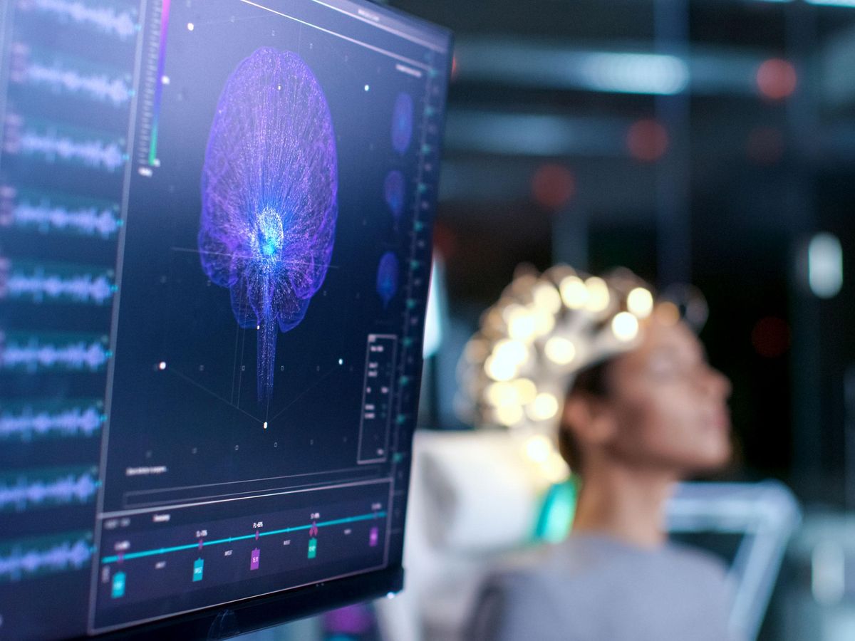 monitor with brain scan in foreground, woman with electrodes on head in background