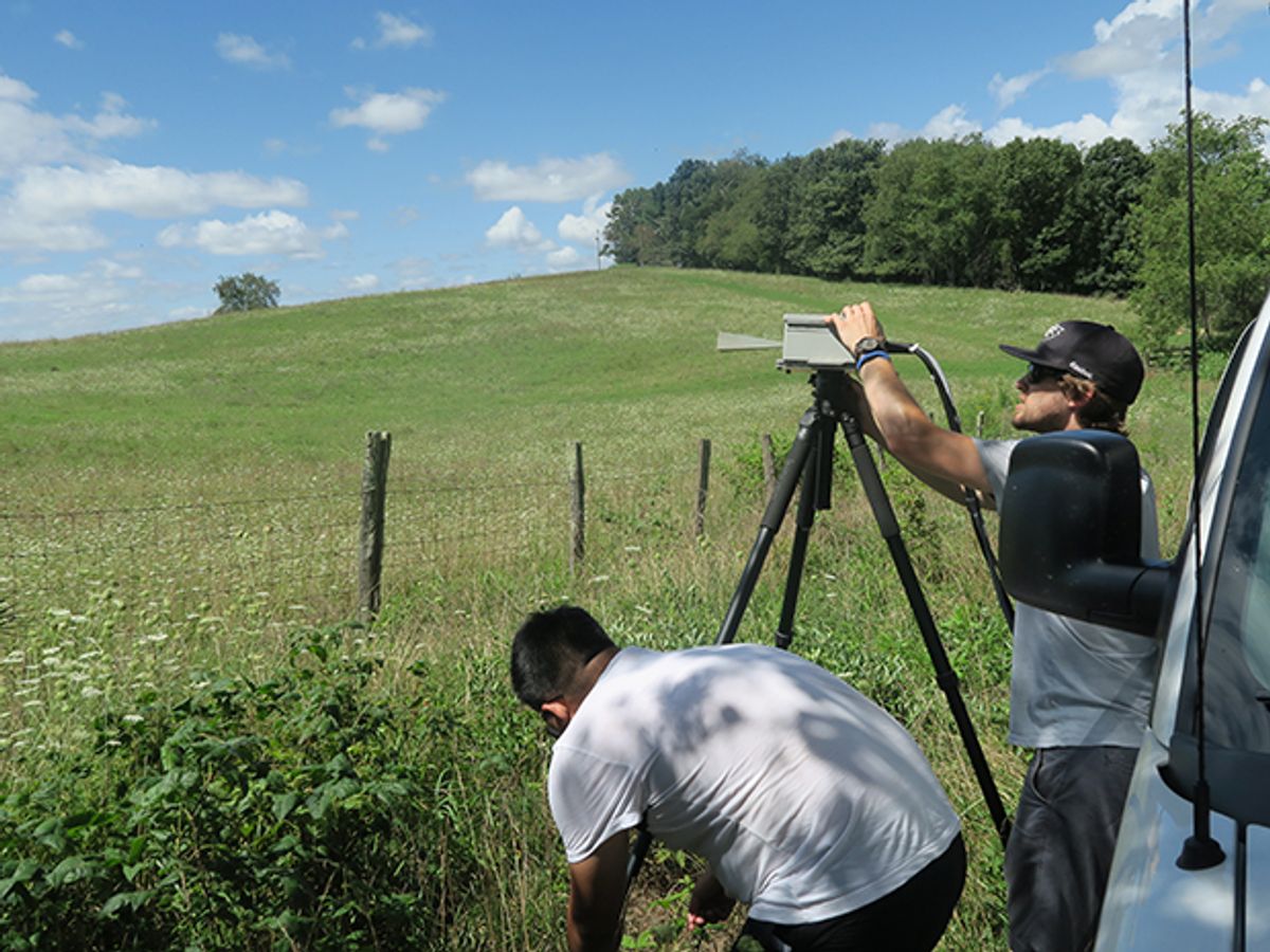 NYU students Yunchou Xing and George MacCartney, pictured outside of a van in a rural Virginia field on a clear summer day, adjust the horn antenna of their receiver to find the strongest signal during a millimeter wave measurement campaign in August.