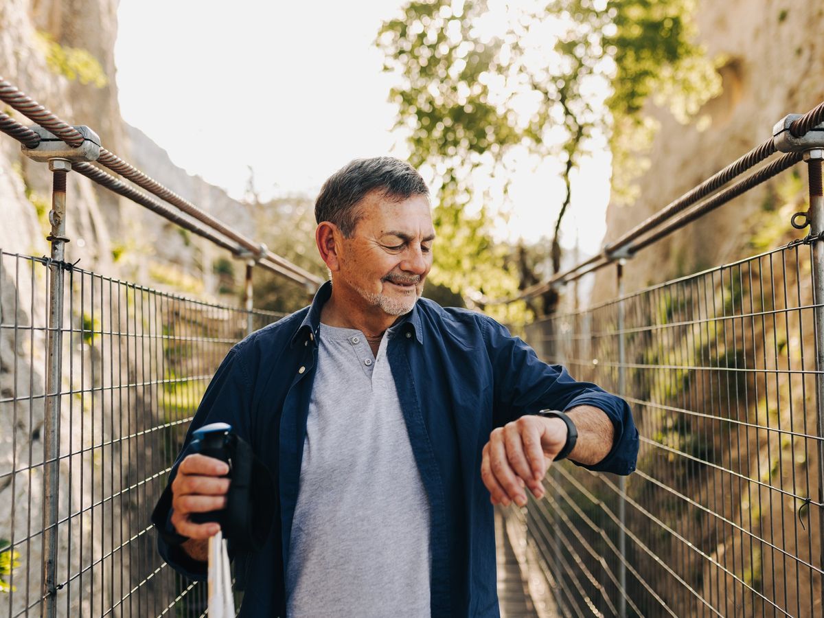 older man looking at smartwatch on wrist and nature in the background