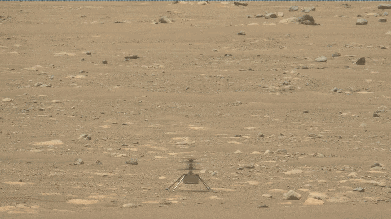 On the dusty, rocky surface of Mars, a distant view of a small helicopter taking off and landing.