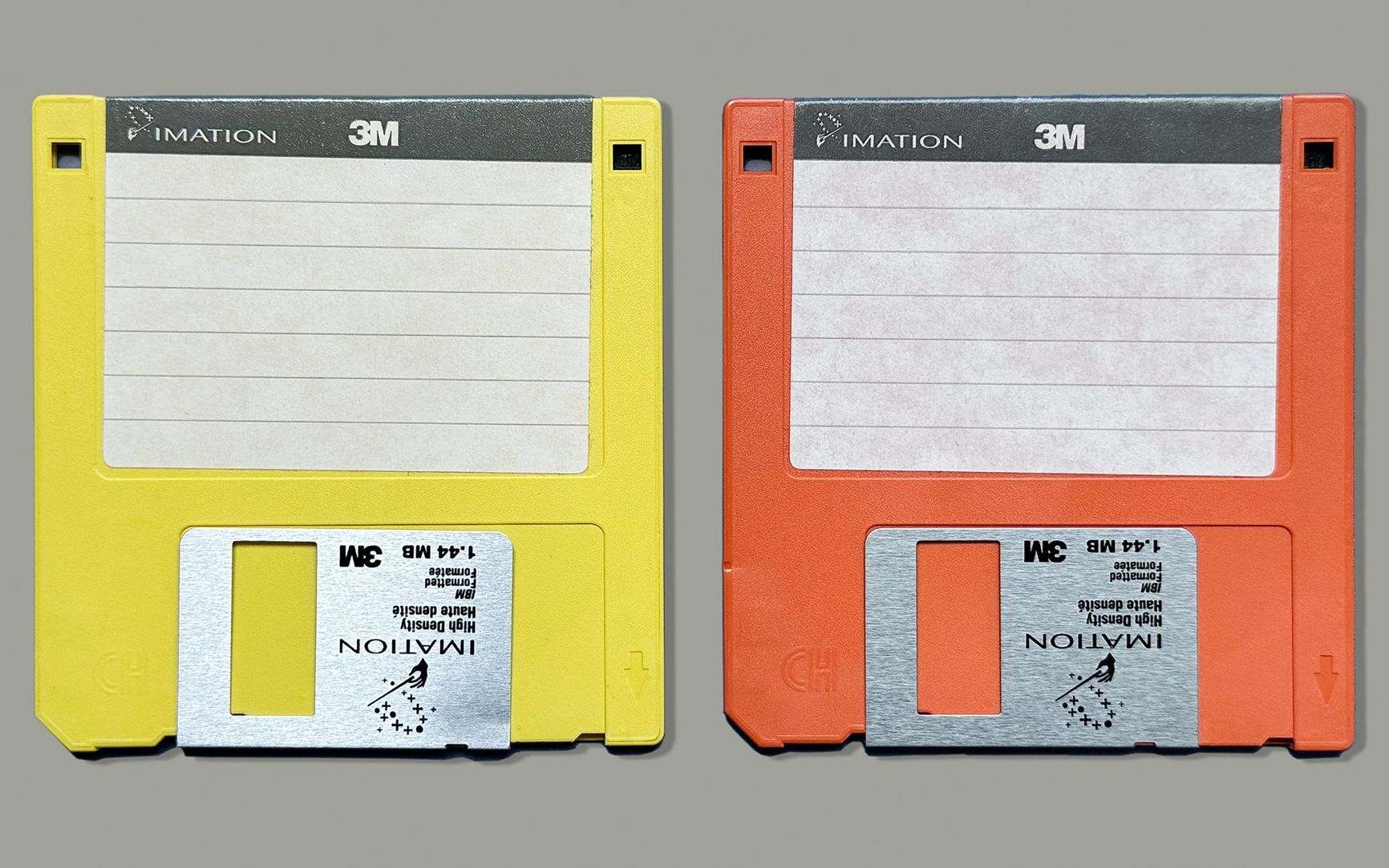 One yellow and one orange Imation 3M 3 \u00bd inch floppy diskettes on a gray background.