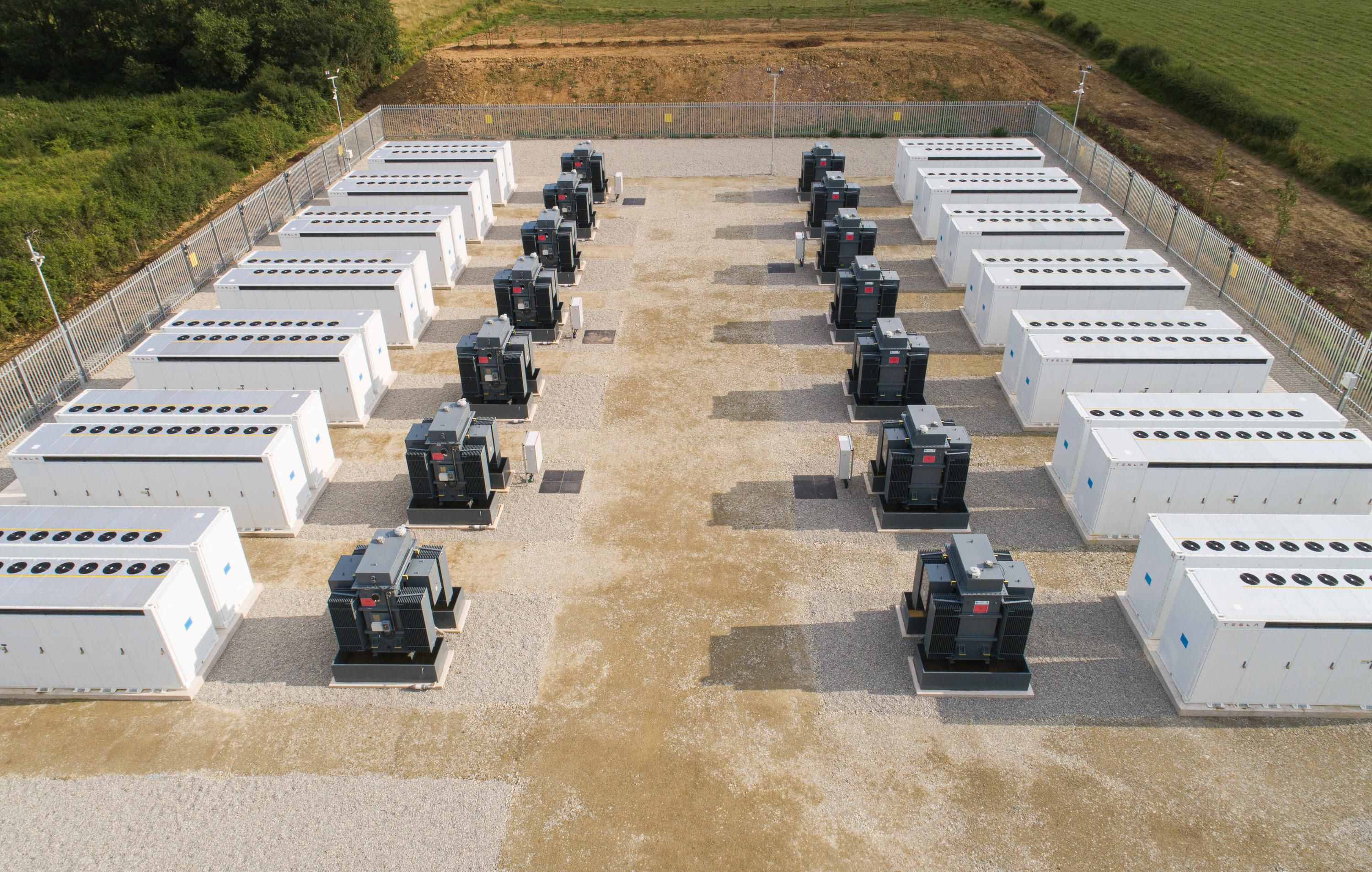 Overhead photo shows 7 large white containers and 7 black and gray large equipment boxes each on the left and right side in a grid. 