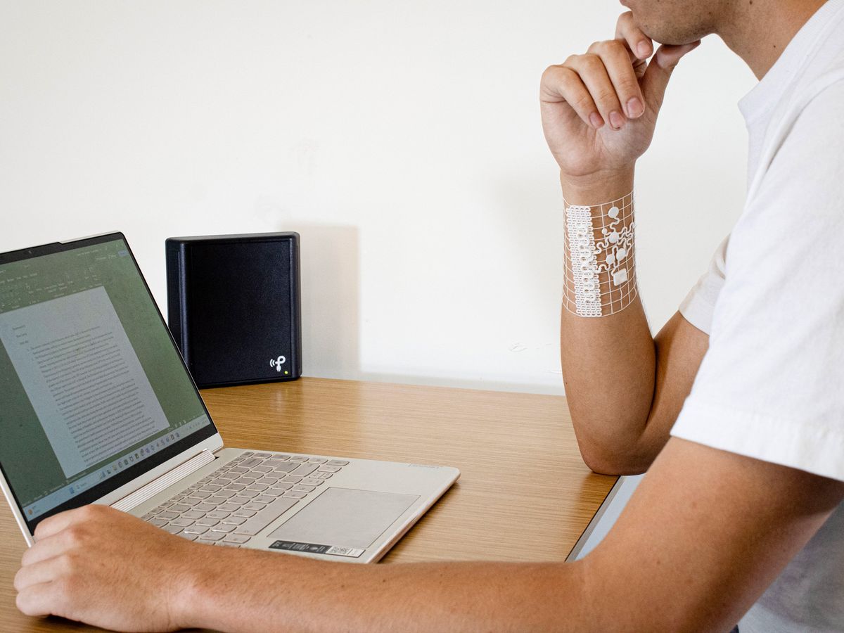 person sitting at a desk with a laptop open and a white mesh bracelet wrapped around their right wrist