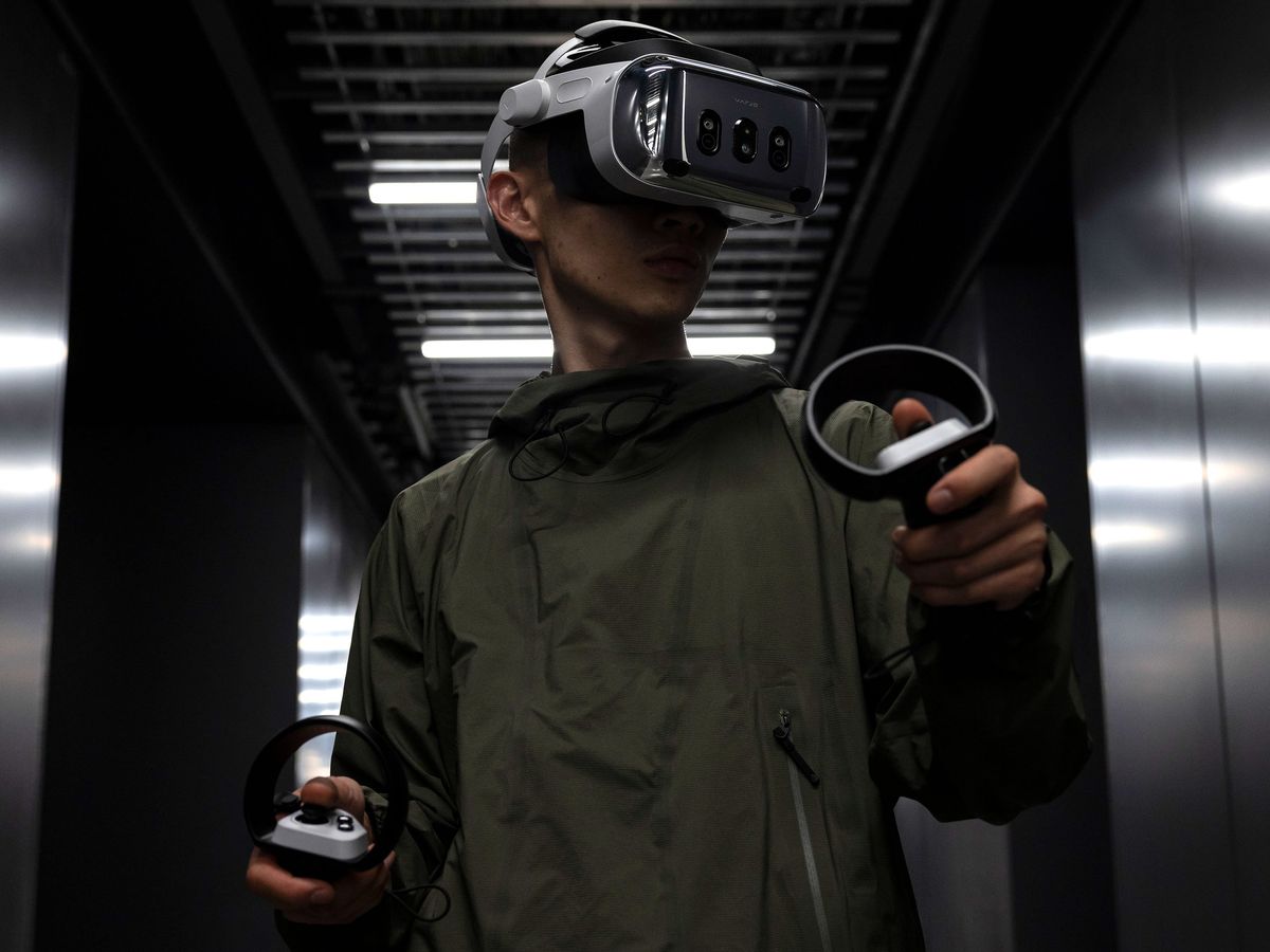 person wearing a virtual reality headset and holding a remote in each hand while standing in a dark hallway