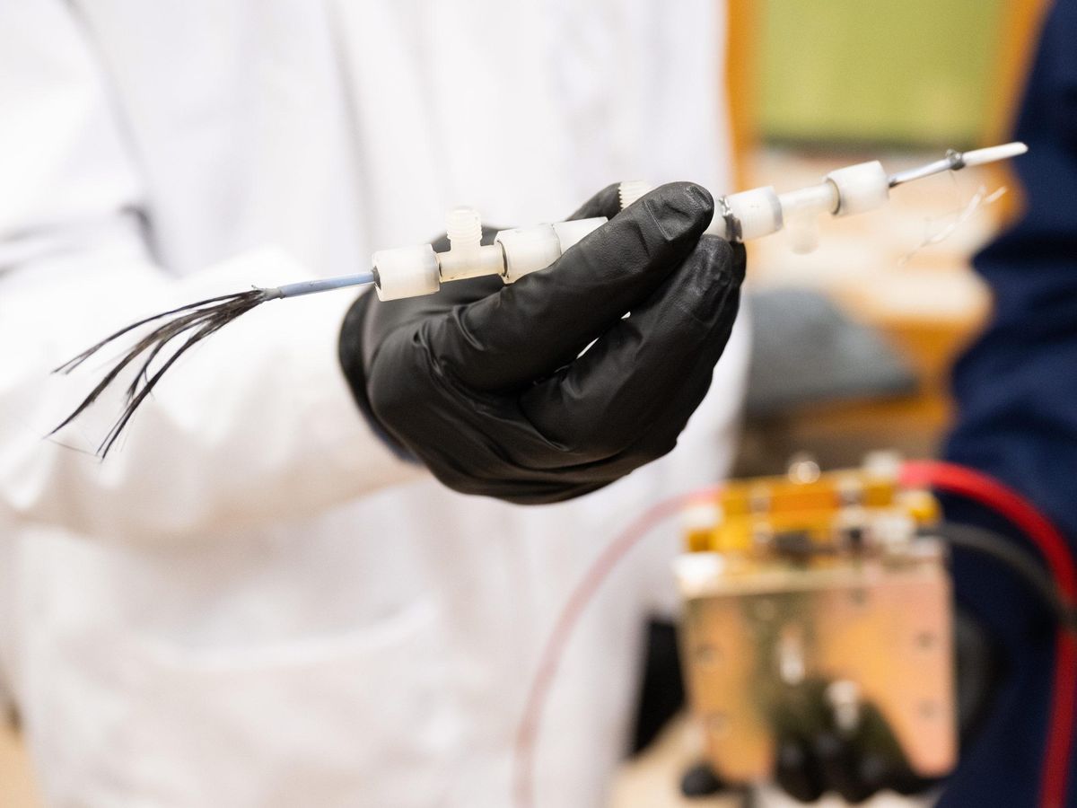 person wearing a white lab coat and black rubber glove holding opaque tube with wire in middle 