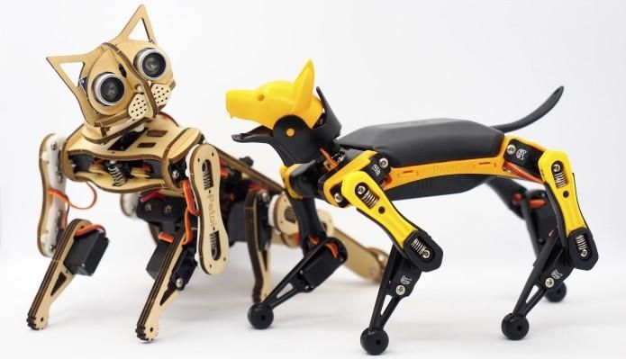Petoi\u2019s quadrupedal robot kits, one made of laser-cut wood and the other plastic, stand next to each other.