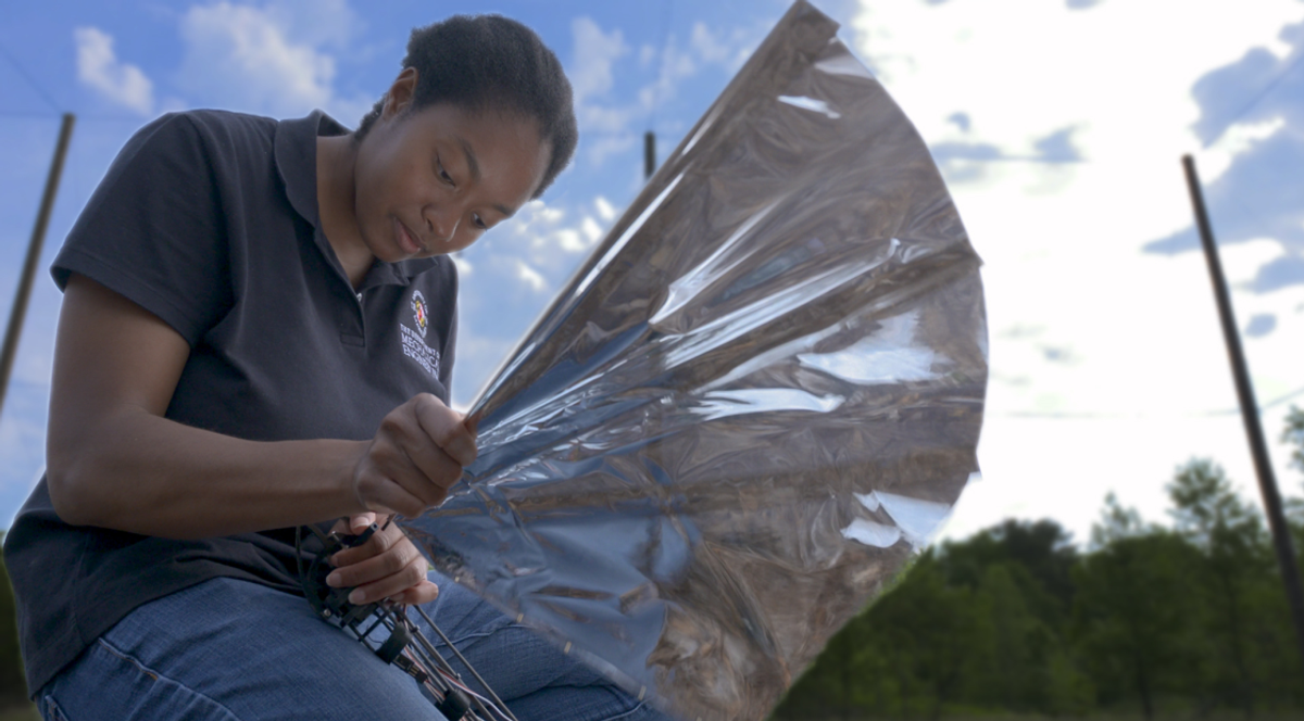 Ph.D. student Lena Johnson kneels to work on the fifth version of Robo Raven, a bird-inspired unmanned aerial vehicle with large silver wings.