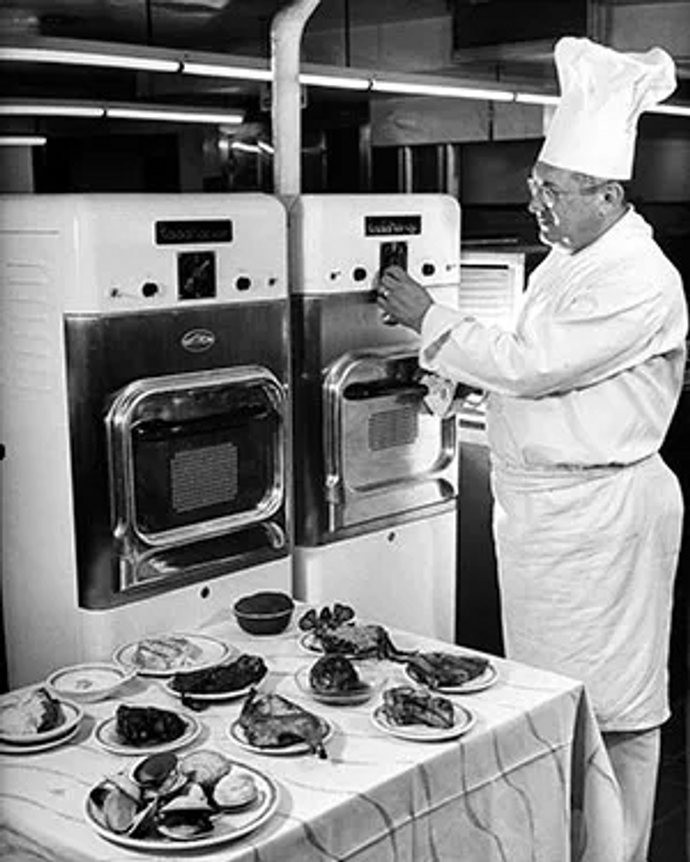 Photo of a chef standing in front of a table of food and microwaves