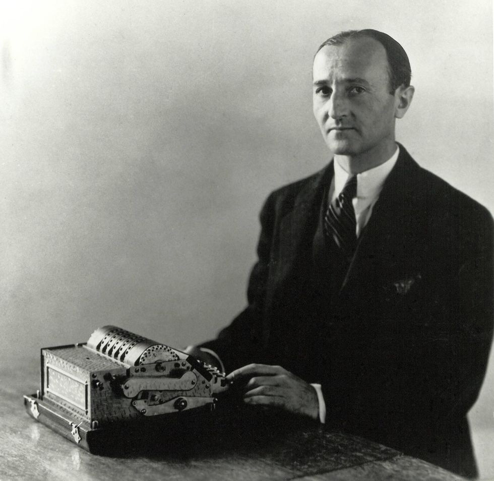 Photo of a man at a desk with his hands on a cryptology device.  