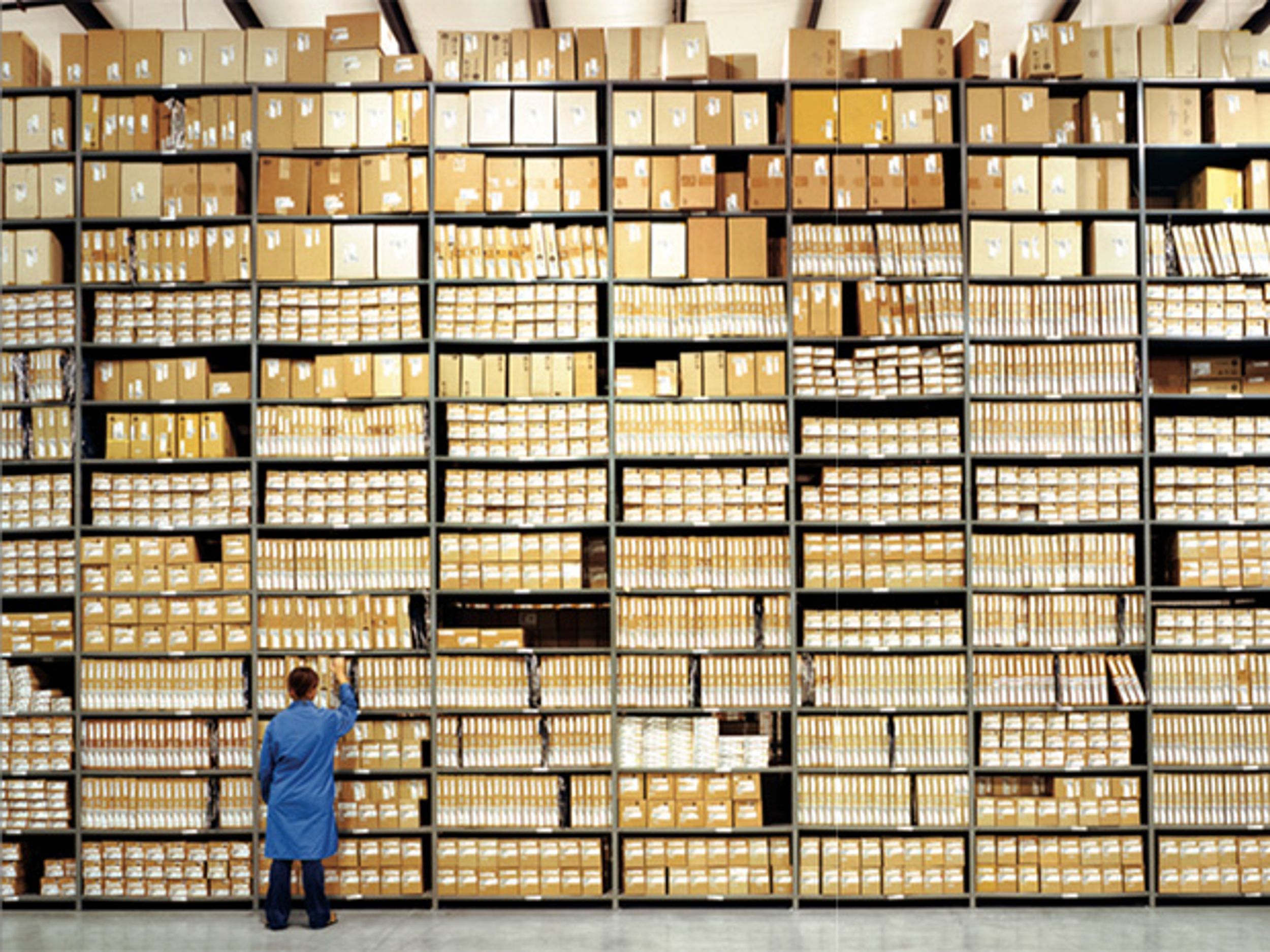 Photo of a man front of a tall shelf of boxes.  