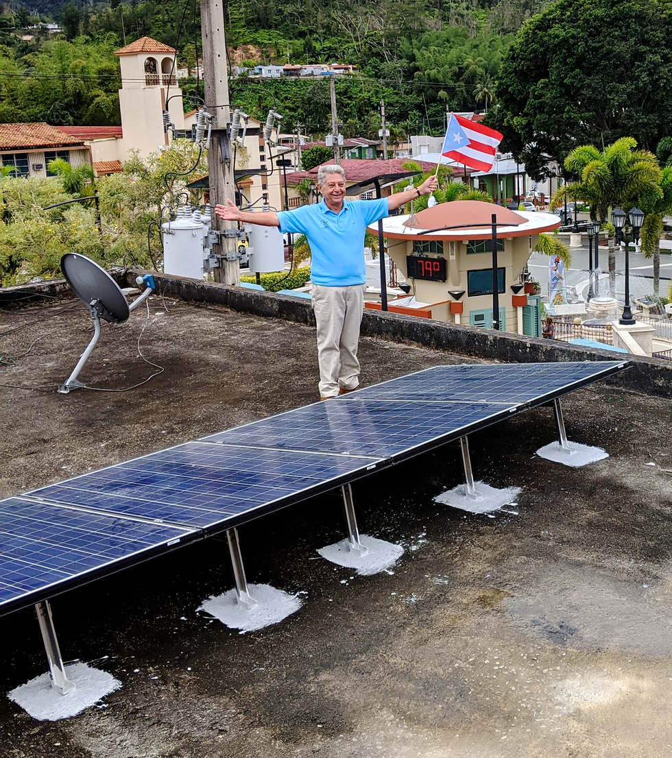 Photo of a man holding a flag standing next to solar panels.