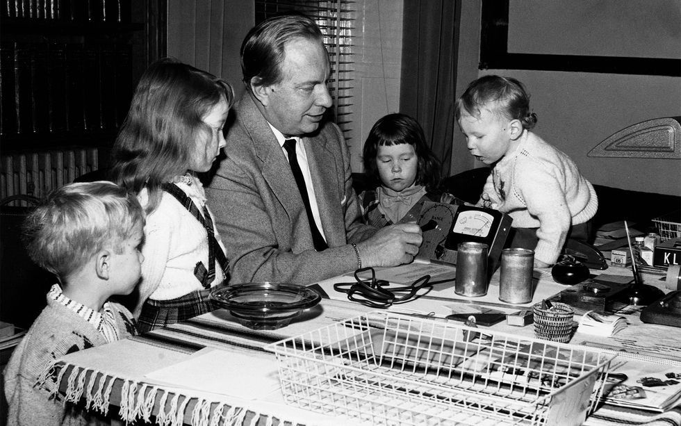 Photo of a man in a suit demonstrating an electrical device to small children.
