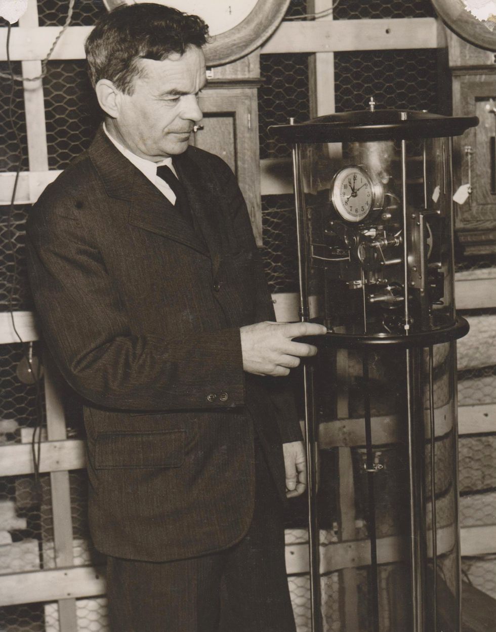Photo of a man in a suit looking at and pointing to a clock apparatus.
