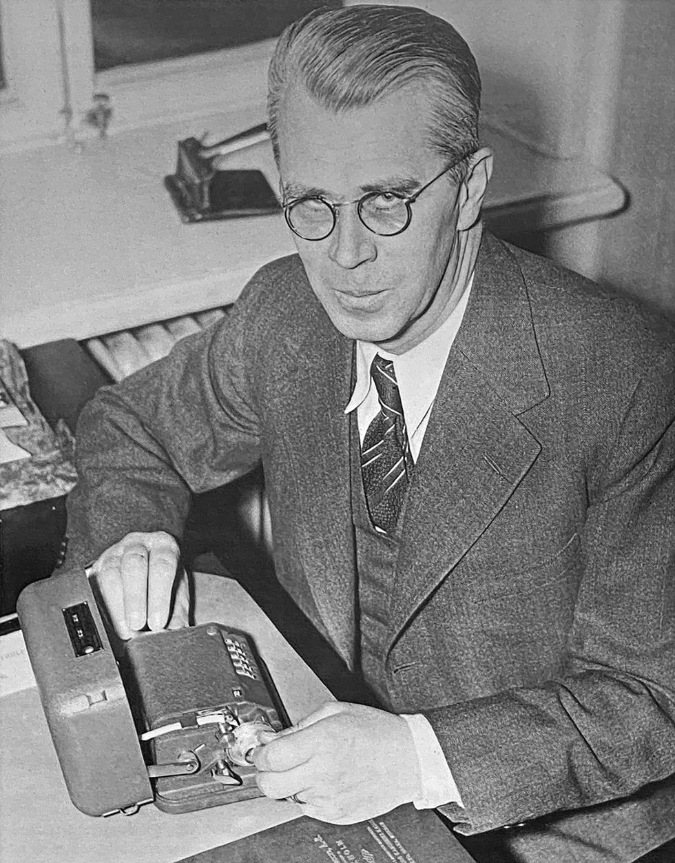 Photo of a man with glasses at a desk with his hands on a cryptology device.  