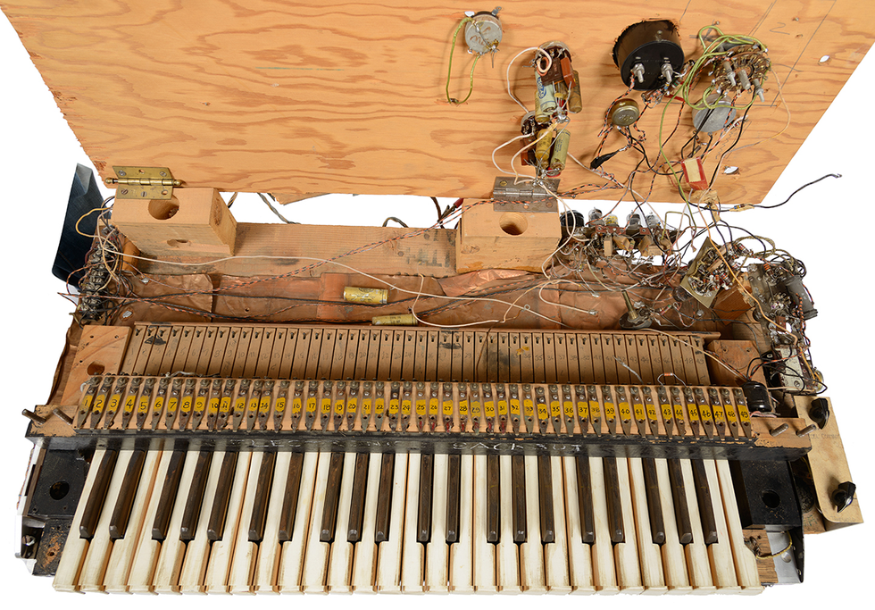 Photo of a musical keyboard attached to tangled wires and electronics mounted on plywood.