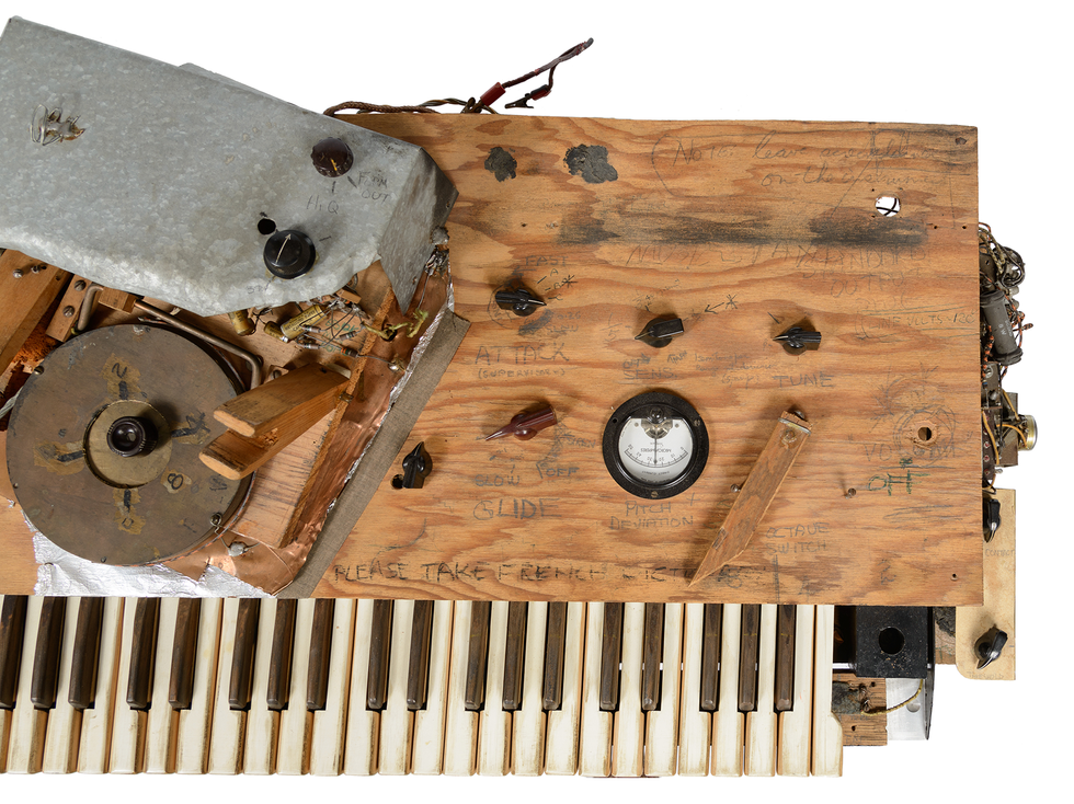 Photo of a musical keyboard instrument showing hand written labels,and assorted electronics.