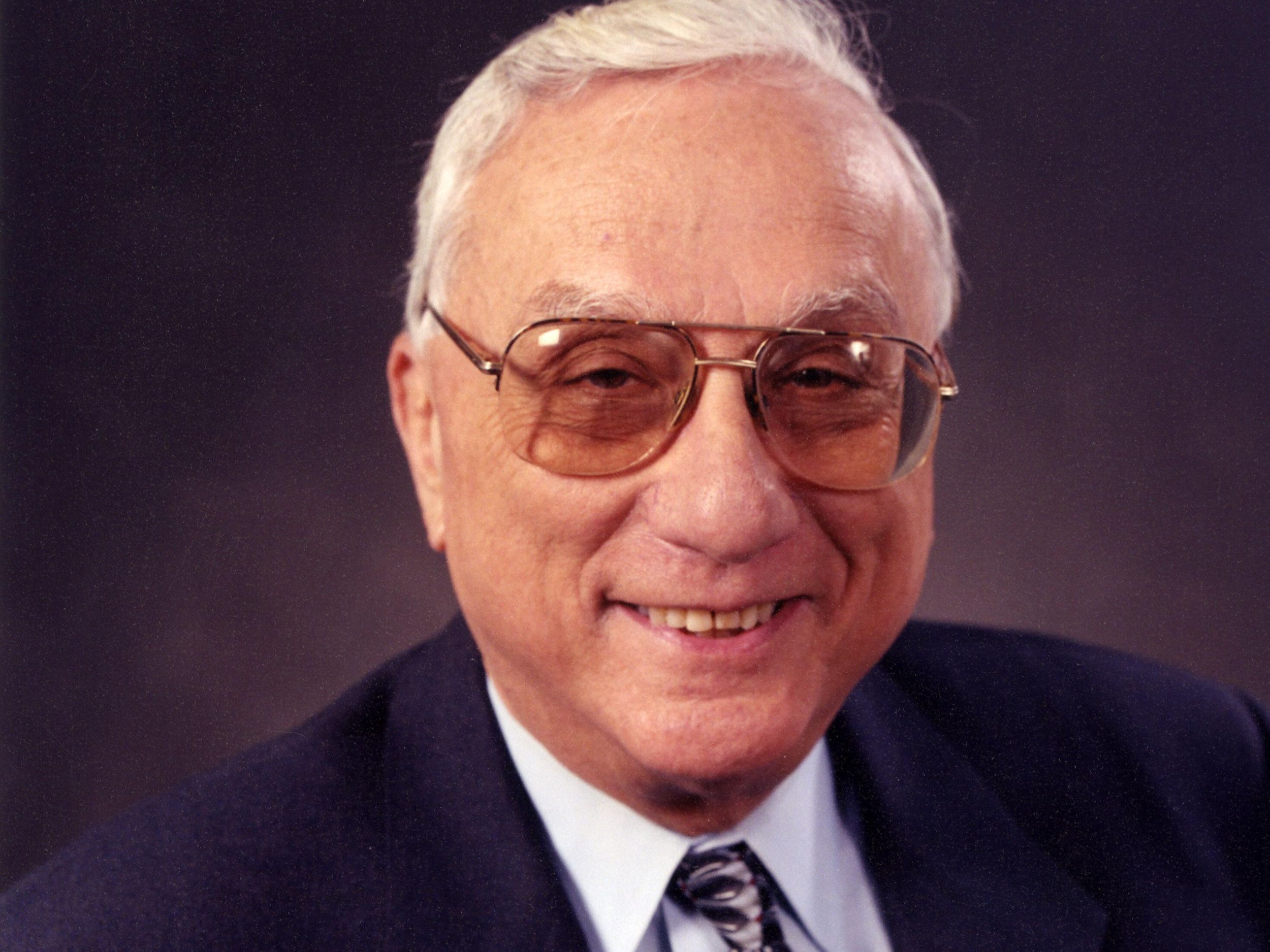 Photo of a smiling man in glasses and a dark jacket.  