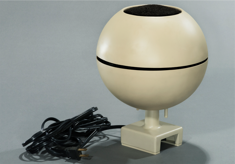 Photo of a spherical off-white object on a small base with an electrical cord to one side.