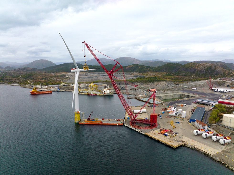 Photo of a wind turbine next to a construction crane in a port.