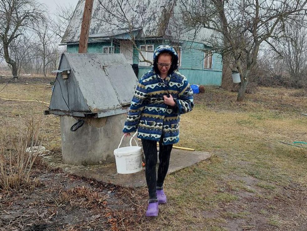 Photo of a woman in a jacket holding a bucket next to a well in a cold and bare landscape
