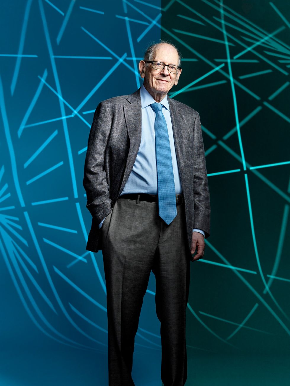 Photo of an older man in a dark suit in front of a blue and green lined background