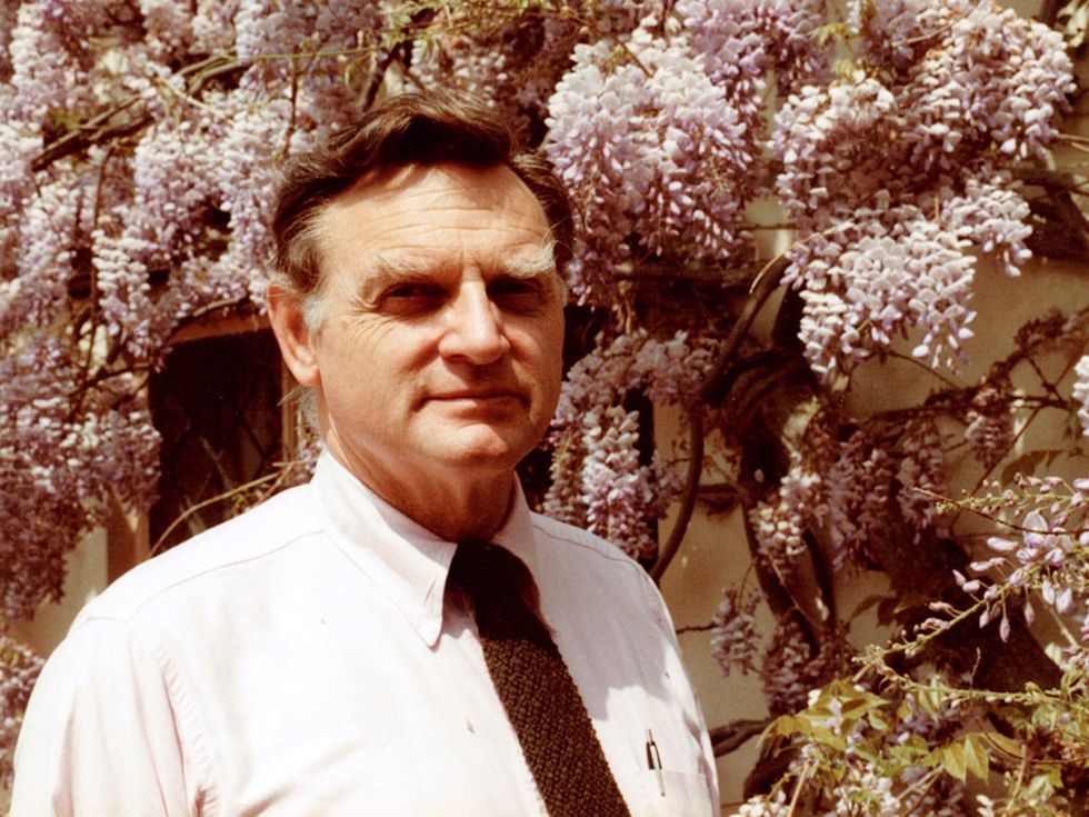 Photo of an olderman in a tie in front of a flowered tree.  