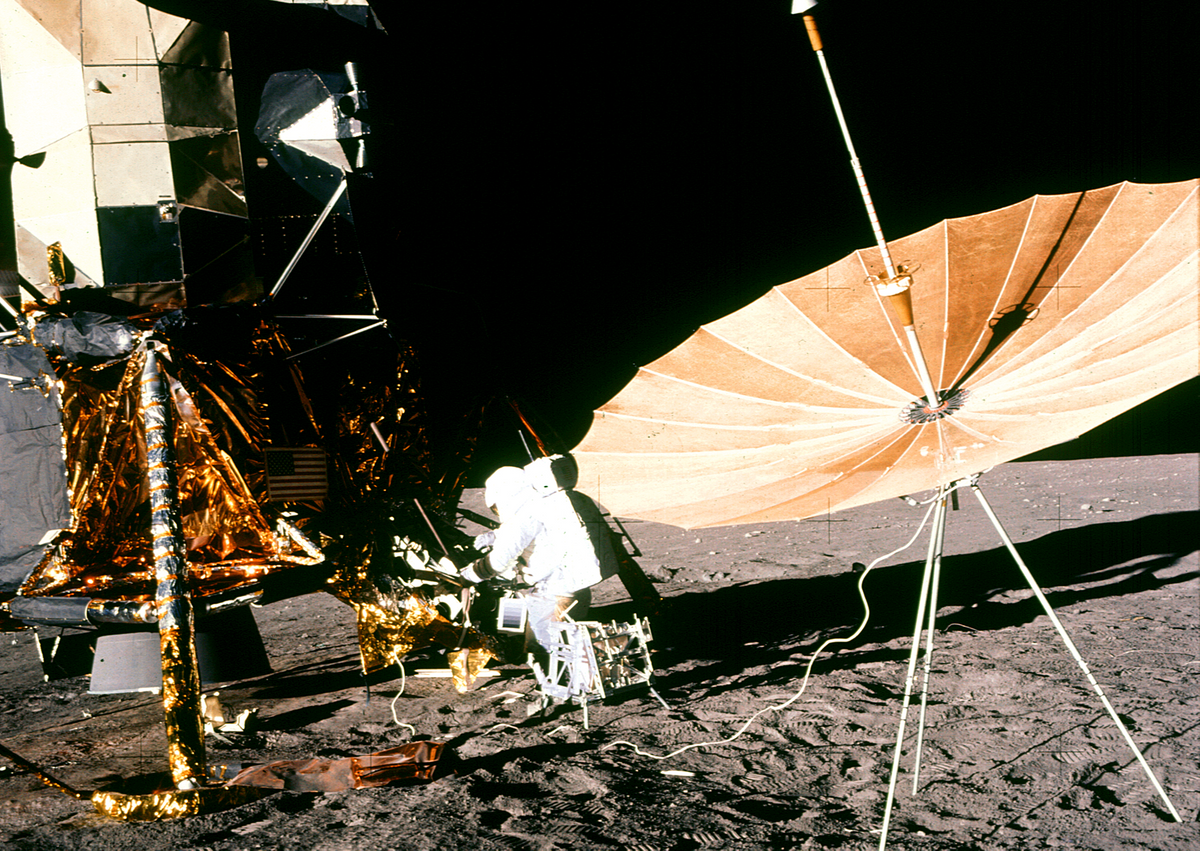 Photo of astronaut on the moon with an antenna in the foreground.  