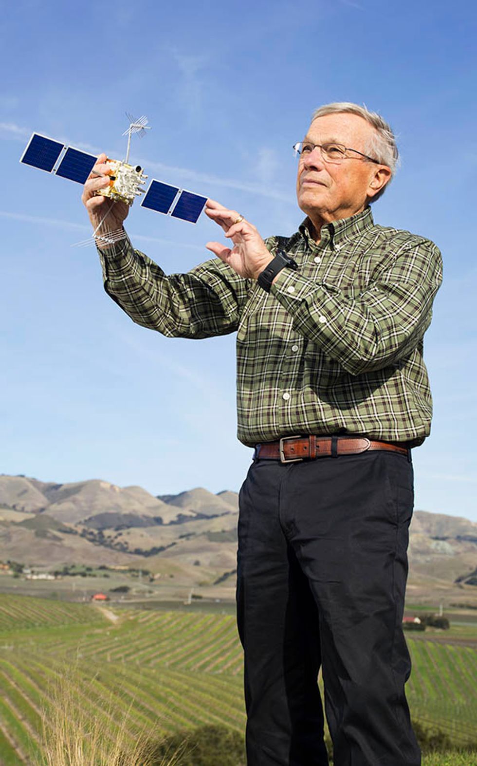 Photo of Brad Parkinson holding a model of the GPS IIF satellite.
