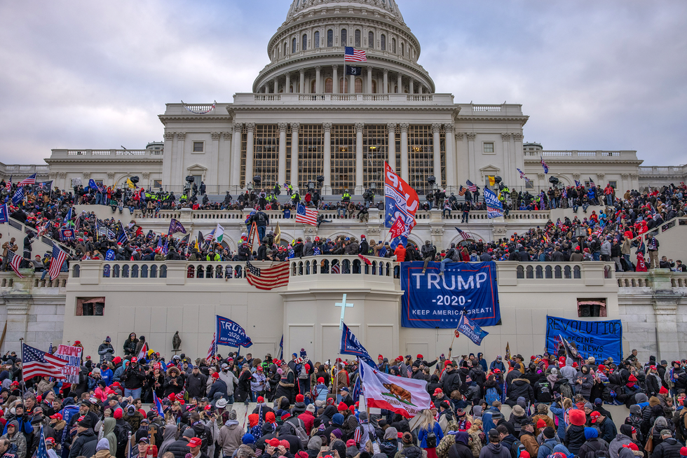 Photo of crowds of people standing in front of the U.S. Capitol Building. Some are holding flags. 