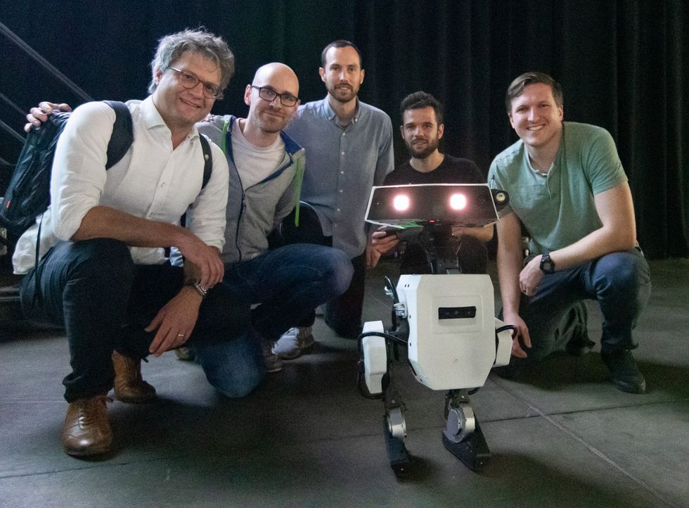 Photo of five men kneeling around a small robot.