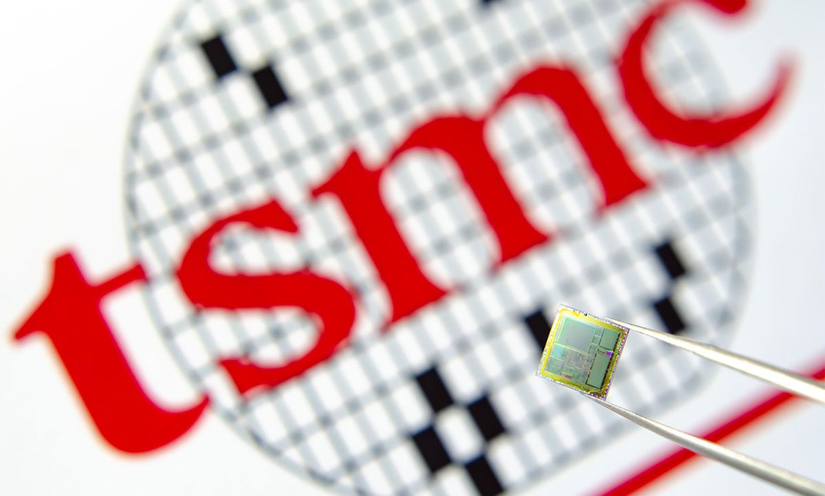 Photo of microchip held in tweezers with TSMC logo on a background.