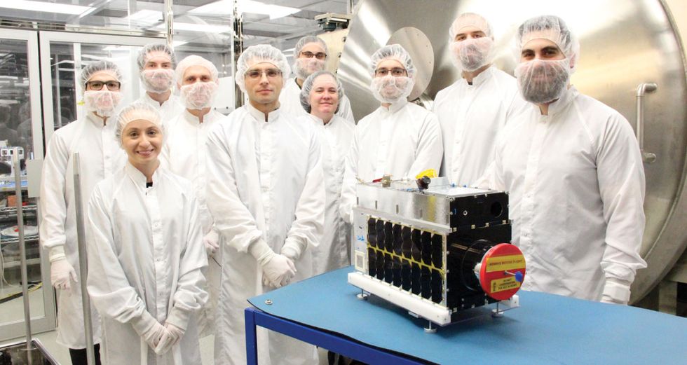 Photo of people in gowns in front of a satellite.  