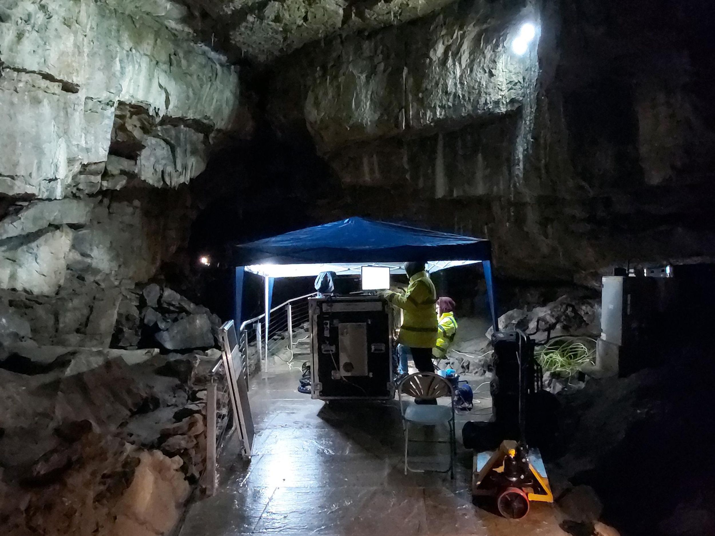 Photo of researchers in an underground geological formation, standing underneath portable tarp with boxes full of equipment