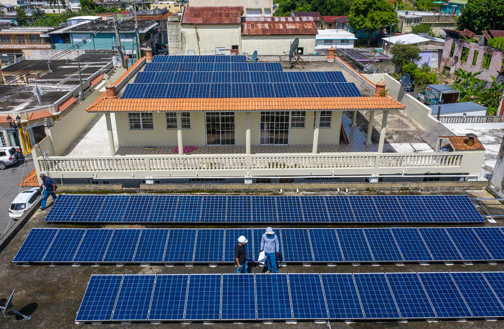Photo of two men standing on a roof near solar panels.  