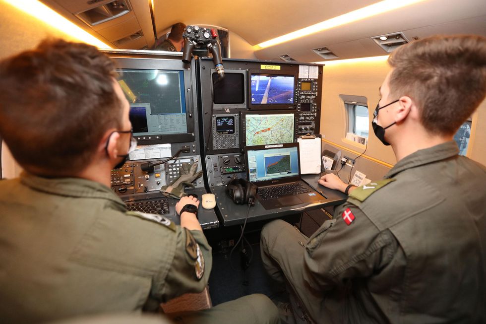Photo of two people in masks sitting in front of screens on a dashboard aboard a patrol aircraft.