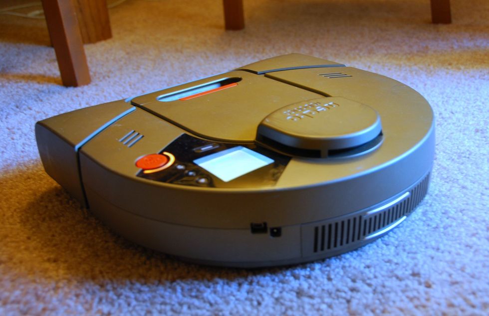 Foto mostrando um robô aspirador em forma de D com um sensor a laser em um carpete.