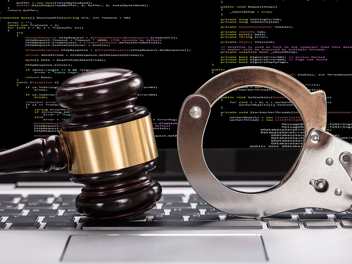 Photograph of a laptop with computer code on the screen, and a gavel and handcuffs on the keyboard.