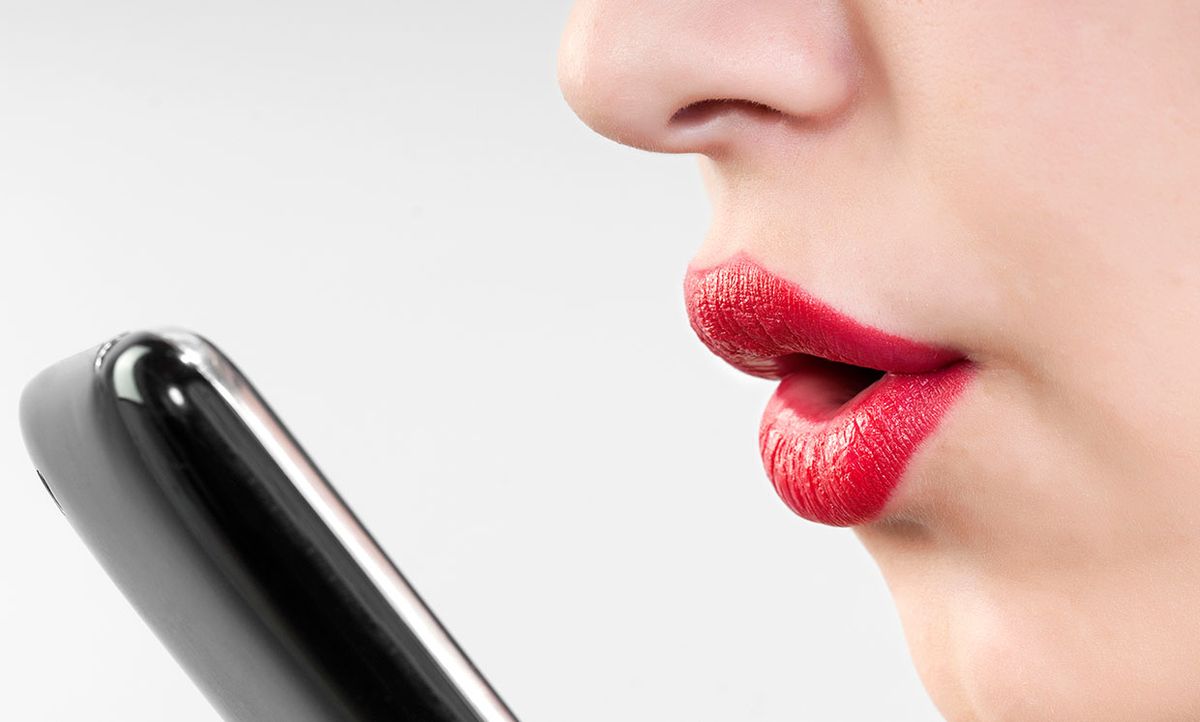 Photograph of a woman's lips near a smartphone.