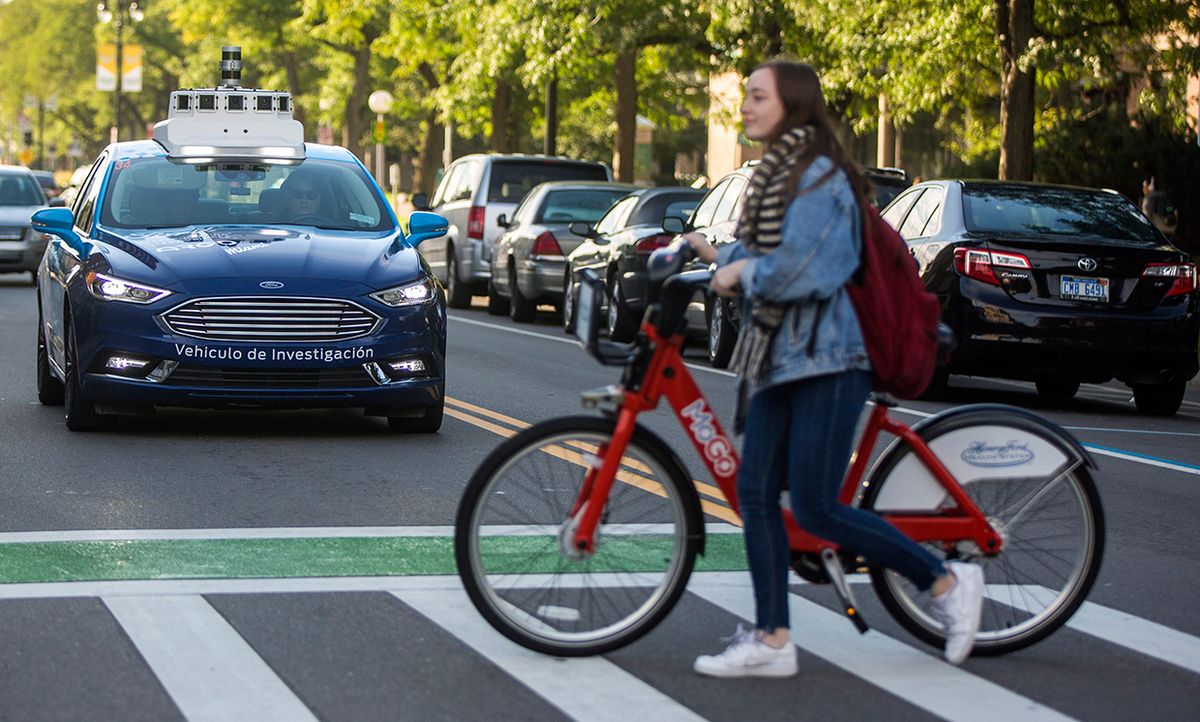 Photograph of Ford's car with the light bar, at an intersection waiting for a pedestrian with a bike to pass.