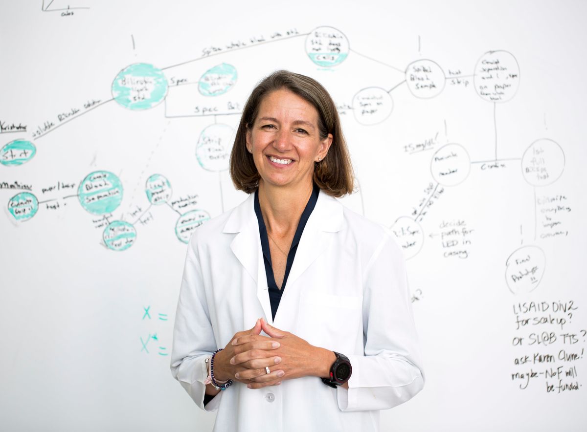 portrait of a woman in a lab coat smiling for the camera with a whiteboard and text in the background